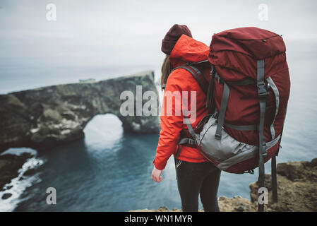 Female hiker wearing red by natural arch in Vik, Iceland Stock Photo