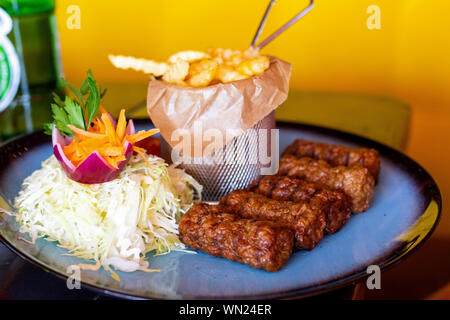 Retro plate of romanian traditional mititei with french fries and cabbage salad Stock Photo