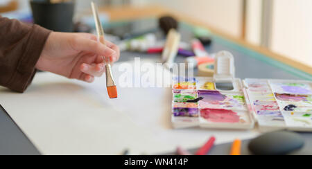 Cropped shot of female artist painting on her project with water colours on grey desk background Stock Photo
