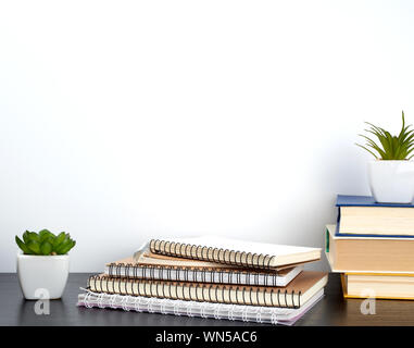 stack of spiral notebooks with white pages and ceramic pots with plants on a black table, white wall, minimalism in Scandinavian style Stock Photo