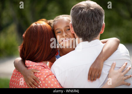 Dark-skinned appealing cute girl hugging foster parents Stock Photo