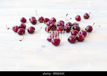 A lot of red berries of sweet cherry scattered on light wooden table close up, bunch of ripe cherry berries on white blurred background macro Stock Photo