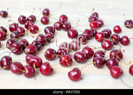A lot of red berries of sweet cherry scattered on light wooden table close up, bunch of ripe cherry berries on white blurred background macro Stock Photo