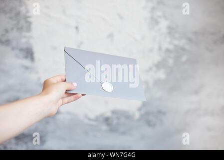 Female hand gives silver envelope a wedding invitation greeting card on a gray background Stock Photo