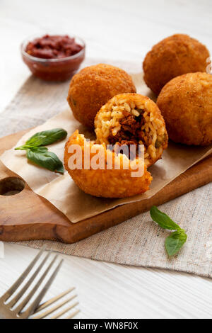 Homemade fried Arancini with basil and Marinara on a white wooden background, side view. Italian rice balls. Close-up. Stock Photo