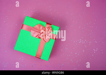 Green gift box with a red bow on a burgundy background with sparkles. View from above. Place for text. Stock Photo
