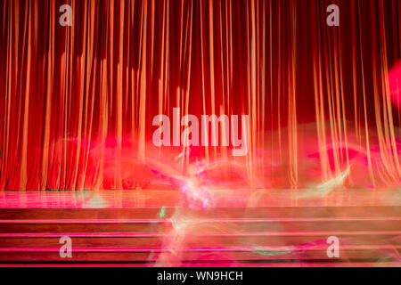 Red curtains and movements of the performers on stage in a theater. Stock Photo