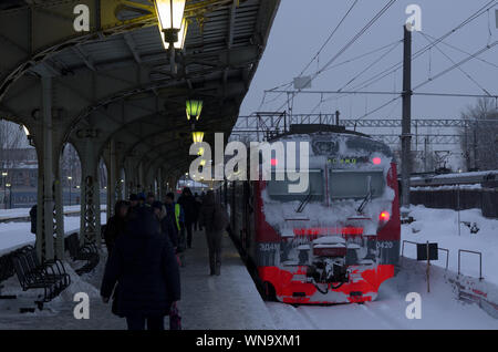 Vitebsky railway station,Saint Petersburg,Russia - January 24, 2019: Red-orange train covered with snow stands near the platform on which people are w Stock Photo