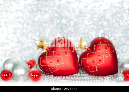 Two red Christmas tree glass balls in the shape of heart with golden stars and silver and red balls on shiny sparkling tinsel background Stock Photo