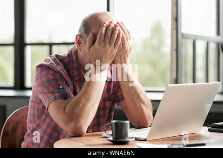 Senior caucasian man rubbing his tired eyes. He is tired to look on laptop screen. Negative facial human emotion about loss of money. Stock Photo