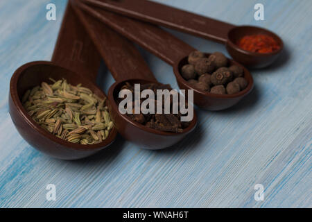 Set of spices - black pepper peas, clove, hot red pepper and exotic spice at the  measuring spoons. bright blue wood background Stock Photo