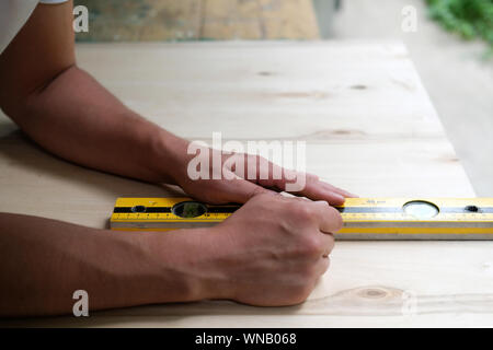 Carpenter marking straight line on plywood sheet using spirit level in carpentry workshop. Measuring, drawing line, DIY concept. Stock Photo
