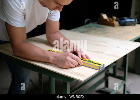 Carpenter marking straight line on plywood sheet using spirit level in carpentry workshop. Measuring, drawing line, DIY concept. Stock Photo