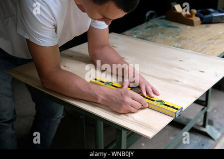 Carpenter marking straight line on plywood sheet using spirit level in carpentry workshop. Measuring, drawing line, DIY concept. Stock Photo