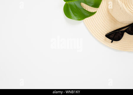 Minimal flat lay style composition with feminine beach straw hat, sunglasses, tropical plam Monstera leaf on white background. Top view, overhead. Sum Stock Photo