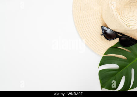 Minimal composition with beach straw hat, sunglasses and tropical Monstera palm leaf on white background. Flat lay, top view, summer vacation concept. Stock Photo