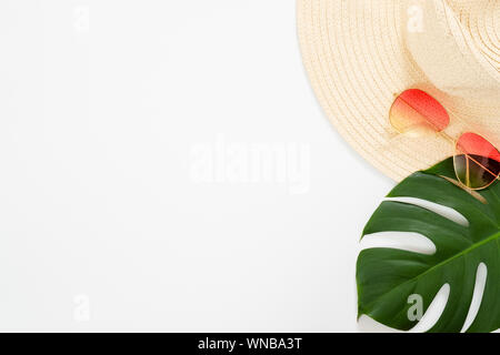 Minimal composition with beach straw hat, sunglasses and tropical Monstera palm leaf on white background. Flat lay, top view still life concept. Stock Photo