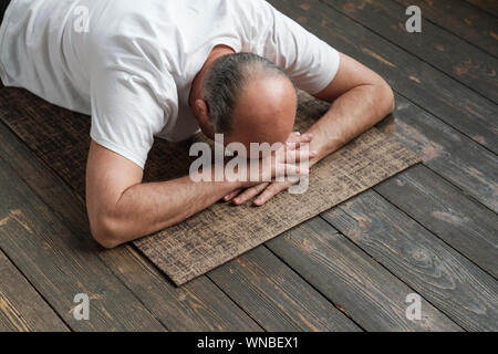Senior aged man resting after yoga exercise on floor. Sports at home for health. Restorative posture. Stock Photo