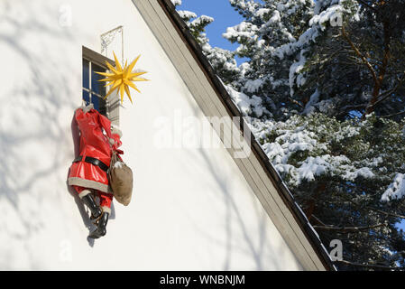 Housebreaker disguised as Santa Clause climbs up a house wall to break in a house through a window Stock Photo