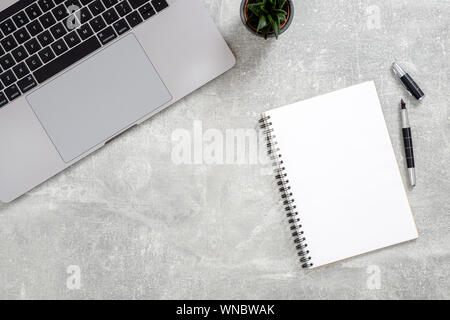 Office desk table with laptop computer, succulent plant, blank paper notepad on concrete stone background. Flat lay, top view workspace Stock Photo