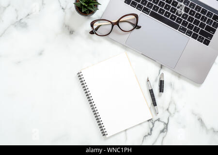 Office desk table with laptop computer, paper notepad, glasses, stationery, succulent plant on white marble surface. Flat lay, top view feminine backg Stock Photo