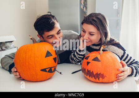Young couple making jack-o-lantern for halloween on kitchen. Man and woman comparing their pumpkins Stock Photo