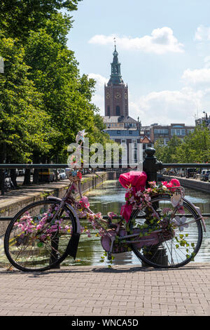 Pink bicycle parking on the bridge over the calm water of a canal with a boat giving a round trip to tourists, Amsterdam, Netherlands