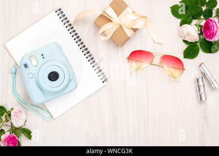 Modern polaroid camera, gift box, sunglasses, feminine accessories, roses on wooden background. Top view, tender minimal flat lay style composition. W Stock Photo