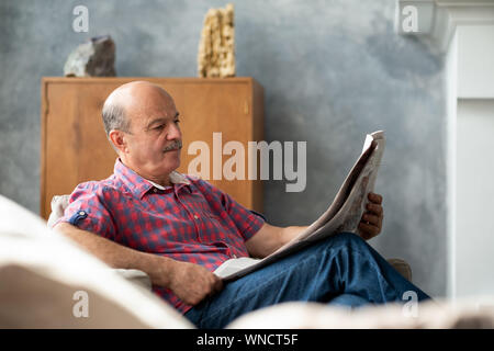 Mature hispanic man reading newspaper at home. Retired father resting in the living room. Stock Photo