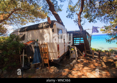 Wild campsite with abandoned old car at forest near sea with beautiful seascape. Summer travel vacation. Freedom lifestyle. Travel destination Greece. Stock Photo