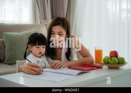 Asian mother playing with her toddler drawing together with color pencils at table in living room at home. Stock Photo