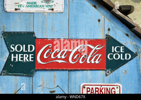a vintage-style embossed metal Coca-Cola arrow sign mounted on a blue vertical wooden plank wall Stock Photo