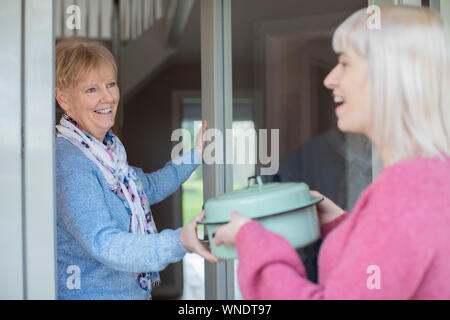 Younger Woman Bringing Meal For Elderly Neighbour At Home Stock Photo