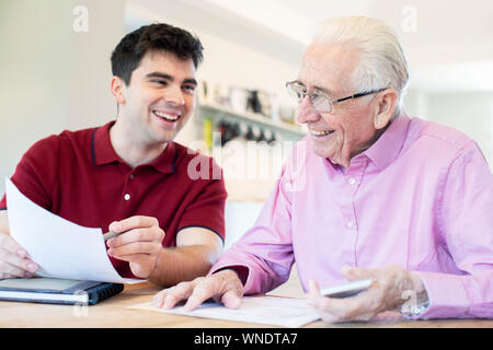 Young Man Helping Senior Neighbor With Paperwork At Home Stock Photo