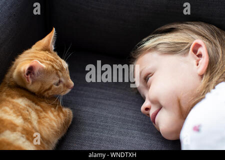 Girl Lying On Sofa At Home Looking Lovingly At Pet Cat Stock Photo