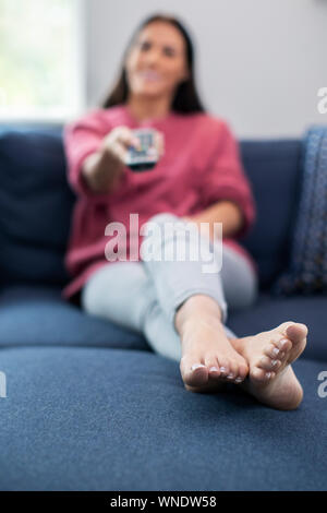 Woman Relaxing On Sofa Holding Remote Control And Watching Television Stock Photo