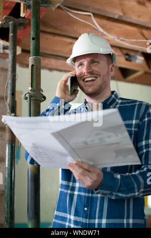 Architect Inside House Being Renovated Studying Plans Talking On Mobile Phone Stock Photo