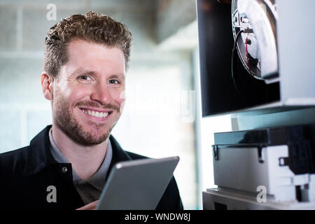 Portrait Of Male Heating Engineer Working On Central Heating Boiler Using Digital Tablet Stock Photo