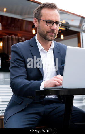 Mature Businessman Working On Laptop By Outdoor Coffee Shop Stock Photo