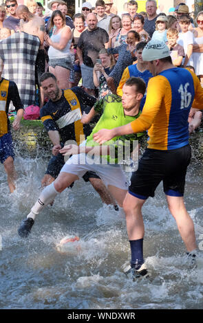 August Bank Holiday festivities in Bourton-on-the Water Gloucestershire UK. The traditional football in the river match. Stock Photo