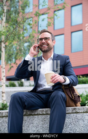 Mature Businessman Taking Phone Call On Mobile Sitting At Outside Office Building Stock Photo