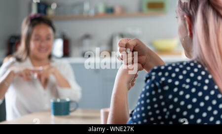 Two Women Having Conversation At Home Using Sign Language Stock Photo