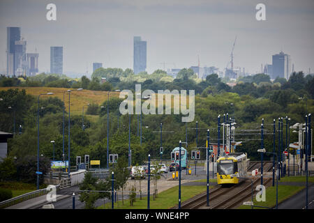 Metrolink tram in Ashton-under-Lyne passing the Ashton Moss Leisure Park (hidden) with Manchester city centre skyline behind Stock Photo