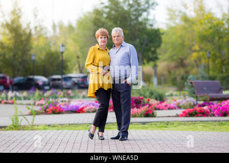 A husband and wife of 60 years old are standing next to each other hugging among the flowers. Stock Photo