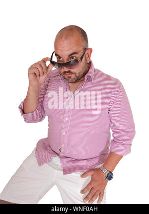 A bald Hispanic man sitting in white shorts on a chair looking over his sunglasses, wondering what is going on, isolated for white background Stock Photo