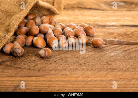 Hazelnuts falling from burlap bag on rustic table Stock Photo
