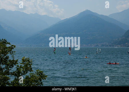 Lake Como, Italy - July 21, 2019: View of mountain lake on a sunny summer day. Windsurfers and a boat passing. District of Como Lake, Alps, Colico