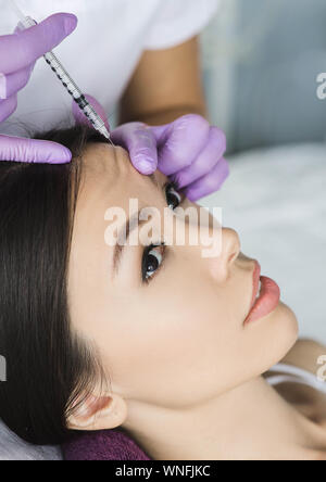 asian woman receiving injection into mimic wrinkle on forehead . Procedure removing wrinkle Stock Photo