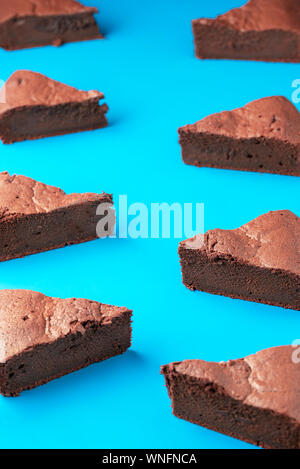 Swedish sticky chocolate cake slices, in a pattern on a blue background. Kladdkaka pieces, symmetrically displayed. Brownie cake portions.