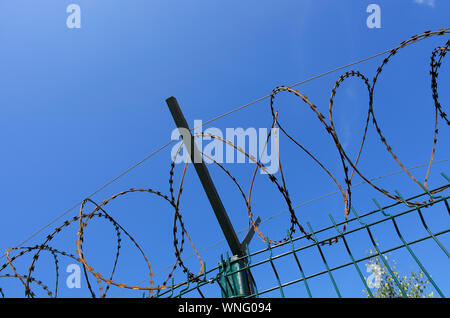 Coils of sharp razor wire on a metal fence with a crossbar closeup